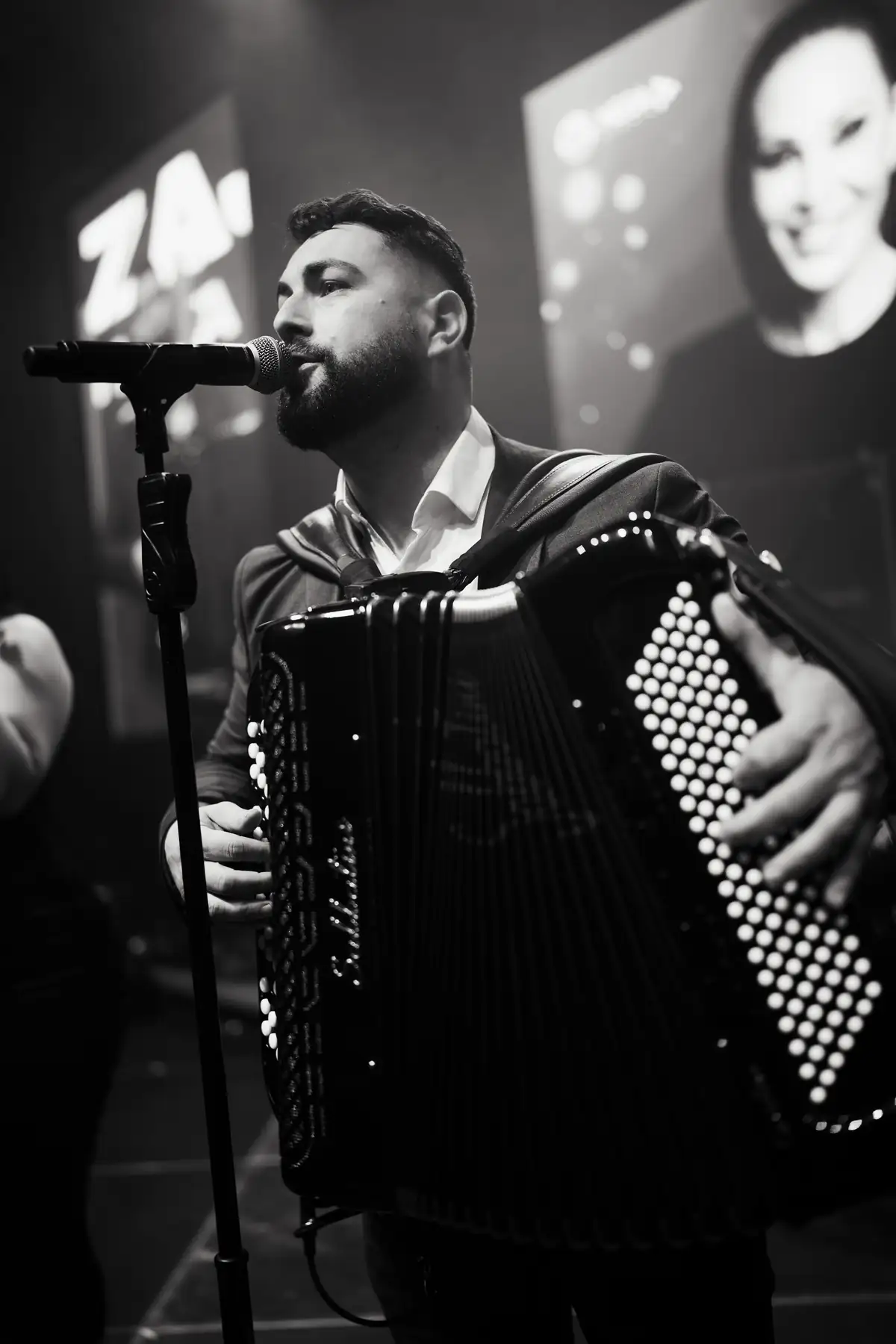 Harmonikaš peva u mikrofon, crno-bela fotografija